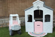 two toys are sitting in the grass near a brick building with a pink door and window