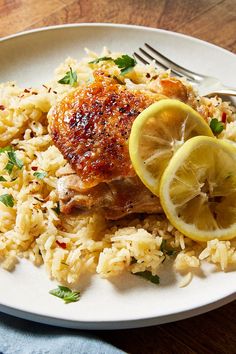 a white plate topped with chicken and rice covered in lemon wedges next to a fork