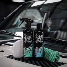 two bottles of liquid sitting on the hood of a car next to a sponge and cloth