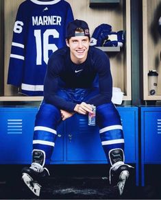 a man sitting on top of a blue locker with hockey jerseys behind him and water bottle in his hand