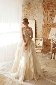 a woman in a wedding dress standing by a brick wall with her hands on her hips