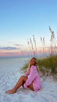 a woman is sitting on the beach with her legs crossed and smiling at the camera