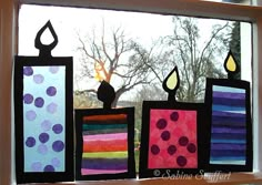 three candles are sitting in the window sill, each decorated with different colored paper