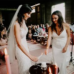 two women in wedding gowns are cutting into a cake with candles on the table