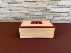 a small wooden box sitting on top of a brown table next to a stone wall