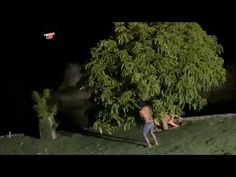 two men are playing frisbee in the grass by a tree at night time