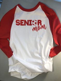 "Senior Mom Shirt - Senior Soccer Mom - Senior Night Shirt - Proud Graduate Shirt - Graduation Mom Shirt - Proud Senior Mom - Soccer Mom Description: What a great shirt for that soccer mom to proudly wear to all the senior year soccer games and senior year events! There are two style options for this shirt 1. 100% cotton, 3/4 sleeve raglan Tee. The example is gray with red sleeves and red graphics, but when ordering please contact me for your own special color requests to match your kids school! White Long Sleeve T-shirt For Sports Season, Sports Long Sleeve Shirt With Letter Print, Long Sleeve Sports Shirt With Letter Print, White Long Sleeve School Spirit Shirt, White Long Sleeve Shirt For School Spirit, White Long Sleeve Sleepwear With Letter Print, White Long Sleeve T-shirt With Team Name, Sporty Long Sleeve Shirt With Letter Print, Red Long Sleeve Tops With Custom Print