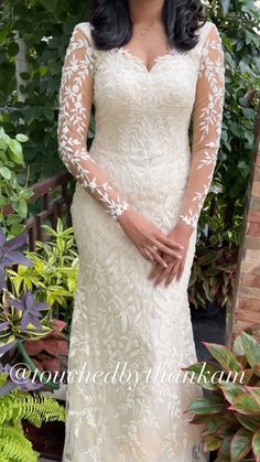 a woman in a white dress standing next to plants and greenery with her hands on her hips