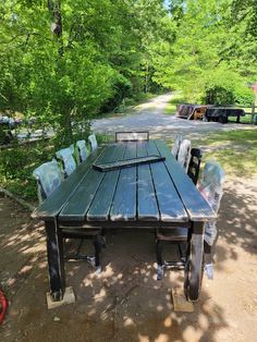 a wooden table and chairs sitting in the middle of a dirt road surrounded by trees