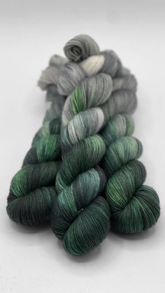 three skeins of green and grey yarn on a white surface, with one skein