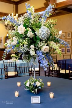 a tall vase filled with lots of flowers on top of a blue table cloth covered table