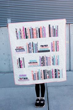 a person holding up a quilt that has bookshelves on it and is standing in front of a building