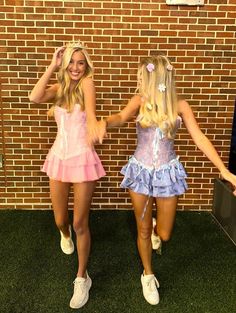 two young women dressed in costumes standing next to a brick wall and holding hands behind their backs