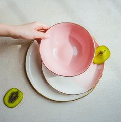 a person is holding a kiwi slice in front of a pink cup and saucer