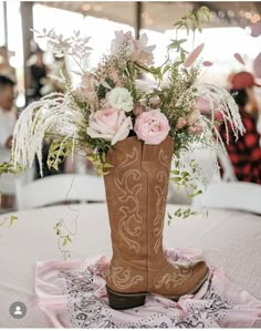 a cowboy boot with flowers in it sitting on top of a pink and white table cloth