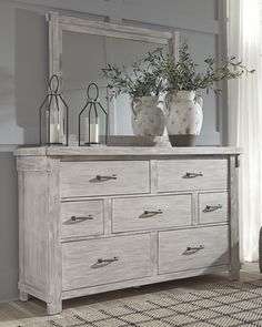 a dresser with two vases on top of it next to a mirror and lamp