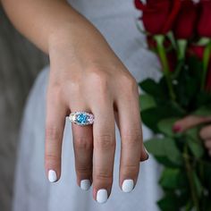 a woman's hand with a ring on it and flowers in the back ground