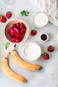 strawberries, bananas and yogurt are arranged on a white surface with green leaves