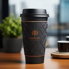 a black coffee cup sitting on top of a wooden table next to a green plant