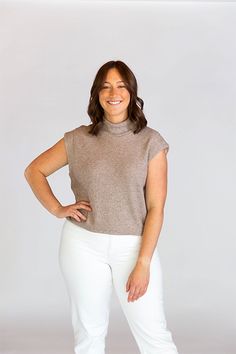 a woman standing with her hands on her hips and smiling at the camera while wearing white pants