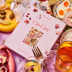 an open book sitting on top of a table next to glasses and plates filled with food