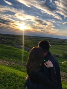 a man and woman standing on top of a lush green field under a cloudy sky