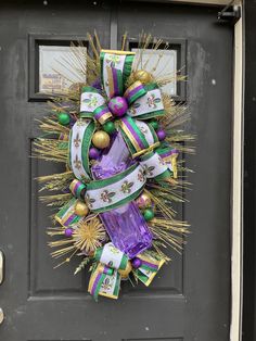 a purple and green christmas wreath hanging on a gray front door with gold ornaments around it