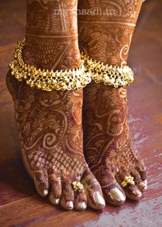 the feet and ankles of a woman with gold jewelry on their legs, both covered in hennap