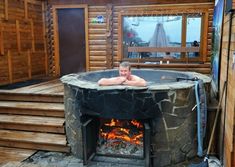 a man sitting in an outdoor hot tub next to a fire place with logs around it