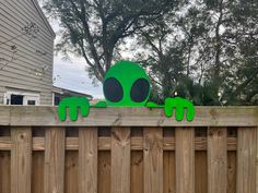 a green alien sitting on top of a wooden fence