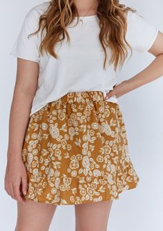 a woman wearing a white t - shirt and brown floral print skirt with her hands on her hips