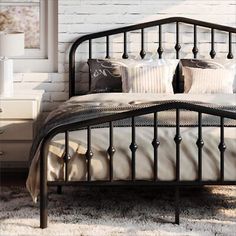 a black metal bed frame with pillows and blankets on top of it in front of a white brick wall