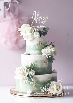 a three tiered cake with white flowers and greenery on the top is surrounded by pink tulle