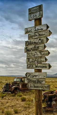 an old truck is parked next to a wooden sign in the middle of a field