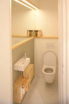 a small bathroom with a toilet, sink and book shelf in the corner by the mirror