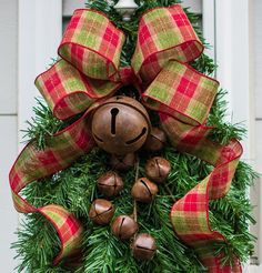 a christmas wreath with bells hanging from it's side on the front door, decorated with red and green plaid ribbon