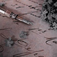 a pen sitting on top of a piece of paper with writing and flowers in the background