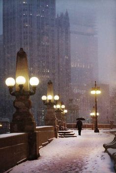 a person with an umbrella walks down a snowy sidewalk in the city at night time