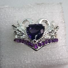 a crown ring with purple and white stones in it on top of a piece of cloth