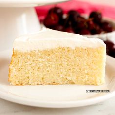 a slice of cake on a white plate with cherries in the bowl behind it