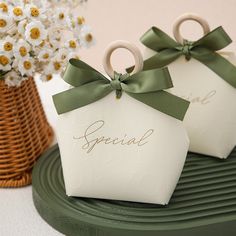 two small gift boxes with ribbons tied around them on top of a green tray next to flowers