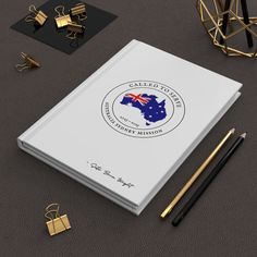 a notebook with the logo of australia on it next to some pens and gold objects