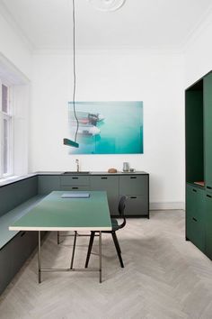 a room with green cabinets and a table in the center, next to a large painting on the wall