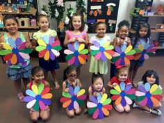 a group of children holding up colorful paper flowers in front of their faces and smiling at the camera