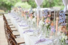 a long table with many vases filled with flowers and candles on top of it