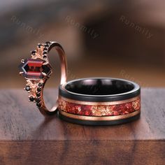 two wedding rings with red and black stones on them sitting on a wooden table next to each other