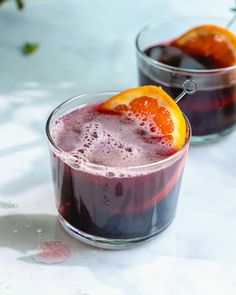 two glasses filled with purple liquid and an orange slice on the rim next to each other