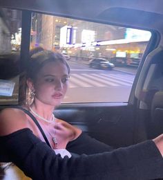 a woman sitting in the driver's seat of a car on a city street