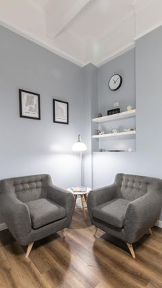 two gray chairs sitting next to each other on top of a hard wood floor in a living room