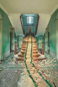 an abandoned building with green and white paint on the walls, stairs leading up to the second floor